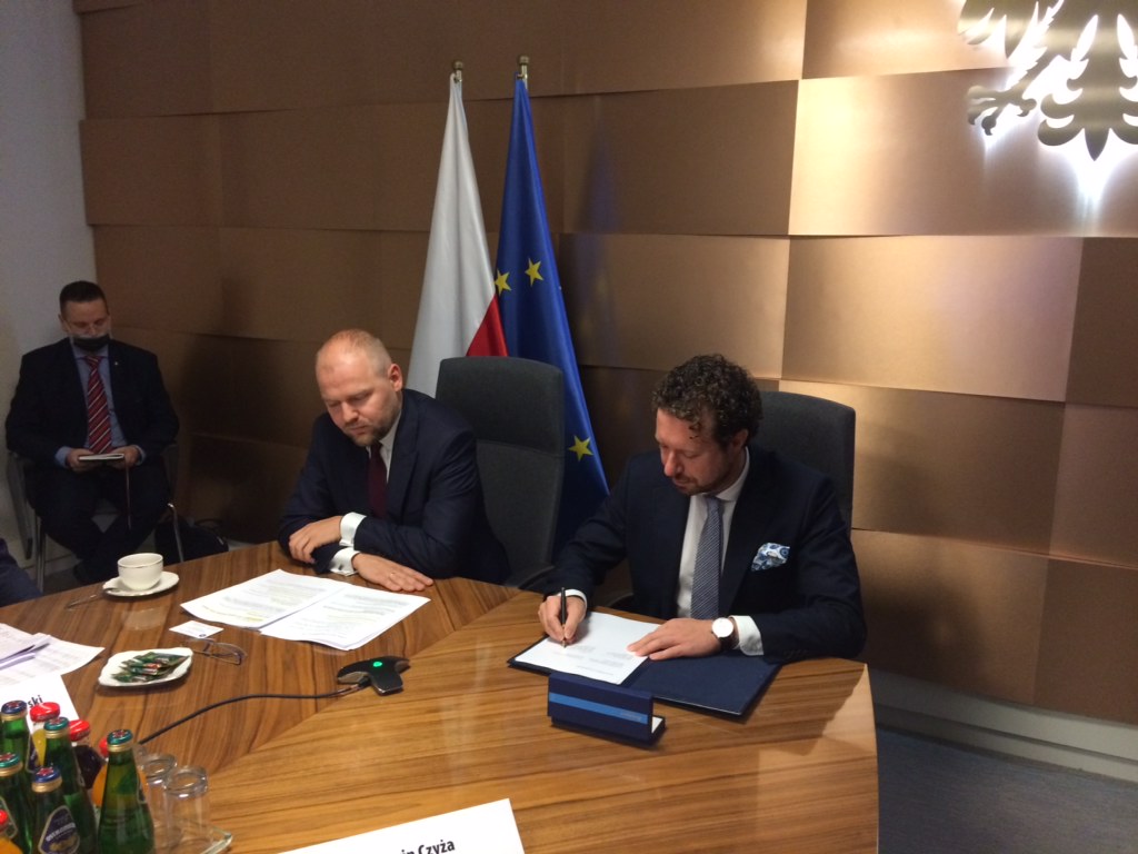Na zdjęciu widać dwie osoby siedzące przy biurku - Marcin Czyża, wiceprezes PARP podpisujący porozumienie w obecności wiceministra rozwoju.