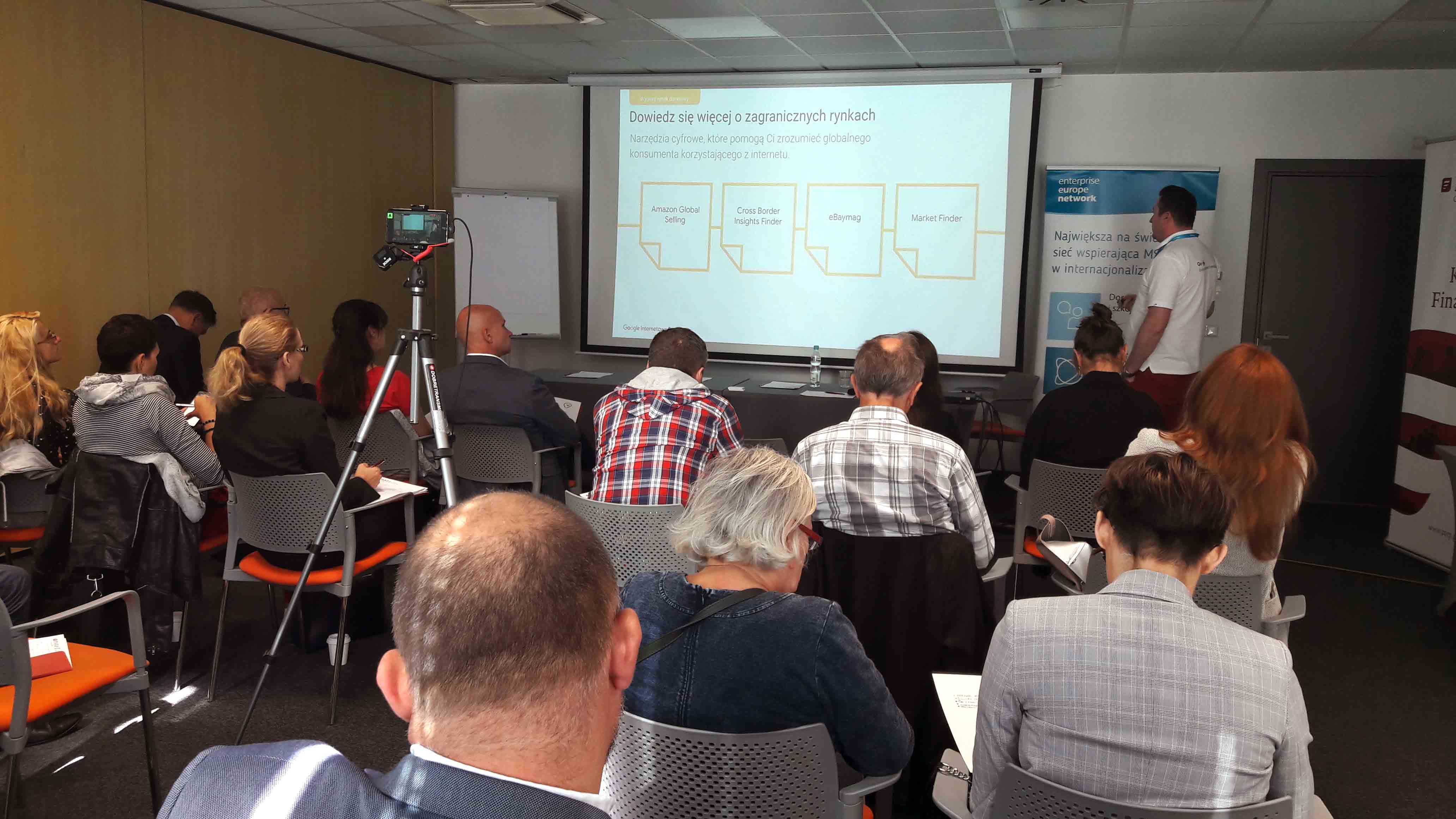 Sala wykładowa. Prowadzący przy ekranie mówi do siedzących uczestników