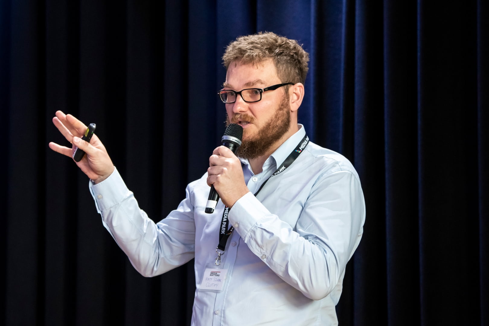 młody mężczyzna z brodą, noszący okulary, trzyma w ręku mikrofon