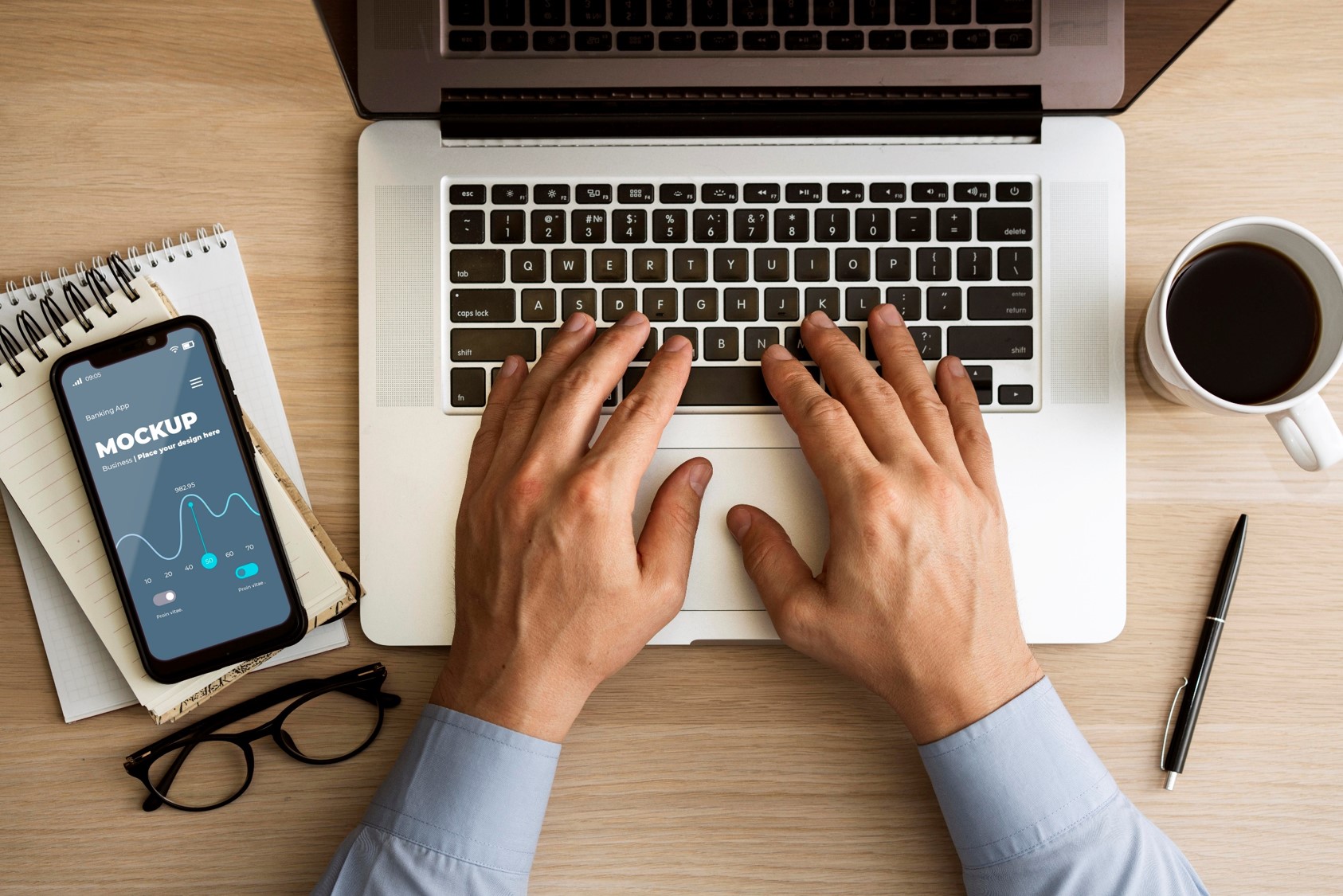 widok z góry na mężczyznę siedzącego przy biurku i piszącego na laptopie. Obok laptopa leży smartfon